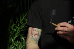 Hombre con camiseta negra con cuello redondo sosteniendo un cigarrillo